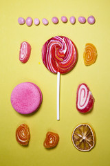 the red lollipop with candy is at at yellow background, sprinkled with sugar