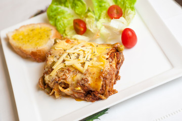 Lasagne on a plate serve with lettuce and garlic bread