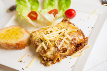 Lasagne on a plate serve with lettuce and garlic bread
