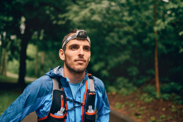 Fit male jogger with a headlamp rests during training for cross country trail race in nature park.