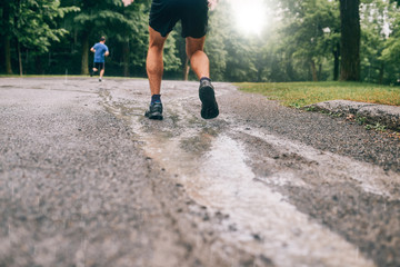 Muscular calves of fit male jogger training for cross country forest trail race in the rain on a...