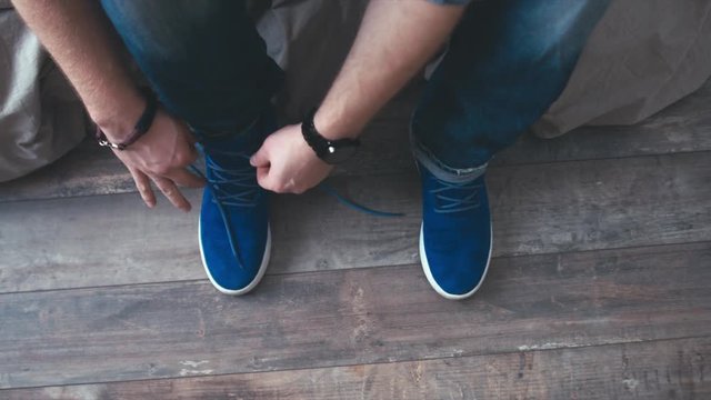 CU Caucasian male tying shoelaces on his blue sneakers. 50FPS SLO MO 4K UHD RAW edited footage