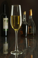 Glass of white wine on mirror table. bottles in a bar on the background