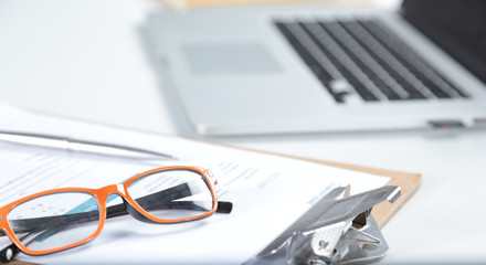 Closeup of white desktop with laptop, glasses, coffee cup, notepads and other items on blurry city background