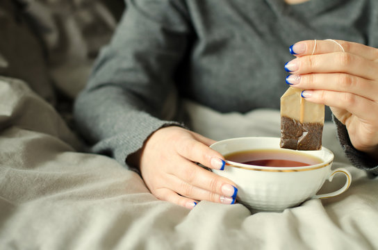 Female hands holding a cup of hot tea on warm blanket.
