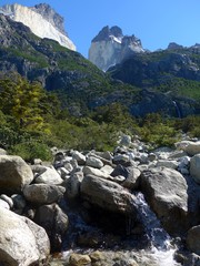 Stream flowing through boulders in front of the massive granite towers and forest of the Torres del Paine National Park.