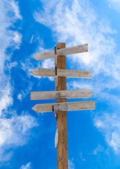 Old Wooden Arrow Signpost Against Blue Cloudy Sky