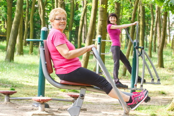 Fototapeta na wymiar Senior and young woman exercising upper and lower body on outdoor gym, healthy lifestyle