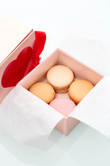 4 colorful macaroons wrapped in the Valentine's Day themed pink box with red heart and bow on top of the box.