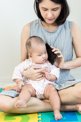 Portrait of a little adorable infant baby girl sitting on mother lap on colorful eva foam and listening to smart phone