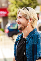 Hipster man standing on city street listening music