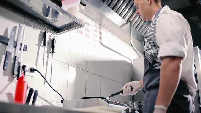 A young man flips a pancake in a frying pan.
