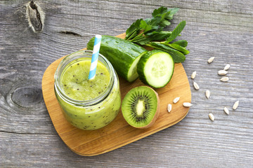 Green smoothie with kiwi fruit, cucumber, mint and parsley on old grey wooden desk