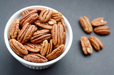 White bowl of pecan nuts. Black background