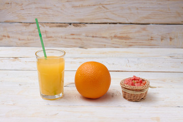 A whole orange with a glass of orange juice on white wooden background with candy in a plate.  Concept.