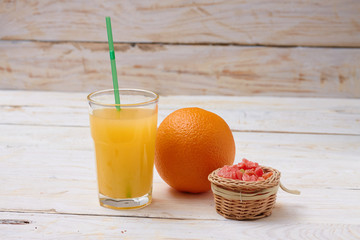 A whole orange with a glass of orange juice on white wooden background with candy in a plate.  Concept.