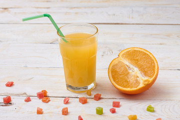 A whole orange with a glass of orange juice on white wooden background with candy in a plate.  Concept.