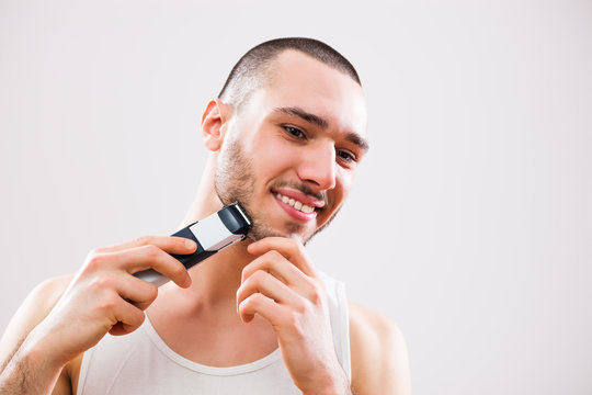 Young man is shaving his beard with electric razor.