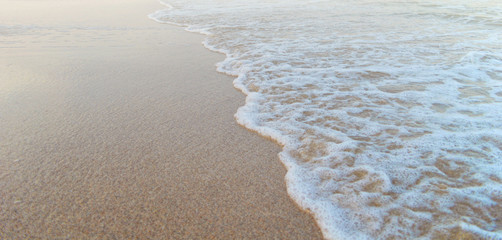 Soft sea waves rolls on golden beach. Foam on sand created by sea waves.