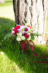 Delicate bridal bouquet with white and red roses of simply supported on the tree on a background of green grass