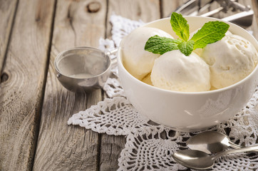 Vanilla ice cream with mint leaves in white bowl on rustic wooden background, selective focus, copy space