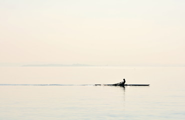 A man with his canoe paddling on the lake; backlit photo, silhouette. - 138165378