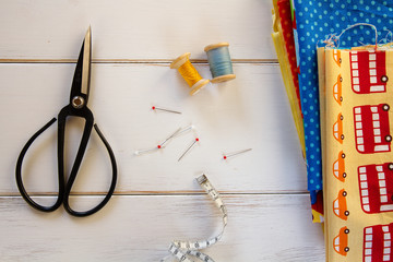 Colorful fabrics with vintage scissors, pins, measuring tape and rolling cotton threads on white...