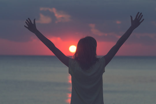 Silhouette of a girl enjoying the sunset / sunrise with arms wide open.
