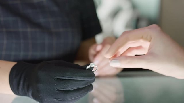 Closeup of female jeweler working at glass counter and giving woman siver ring with diamond to try on