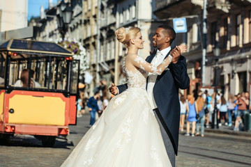 Naklejka premium Happy african American groom and cute bride dancing on street