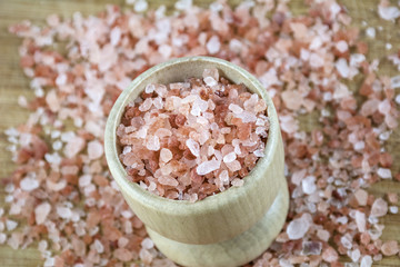 Pink salt in the small wooden bowl on the wooden background