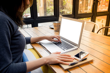 Mockup image of a woman using laptop and presenting with blank white screen on wooden table in modern cafe