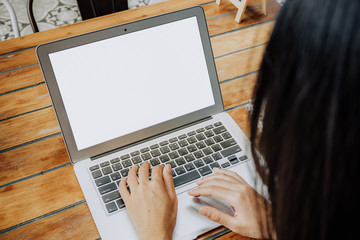 Mockup image of a woman using laptop and presenting with blank white screen on wooden table in modern cafe