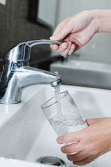 Woman filling a glass of water from a stainless steel or chrome tap