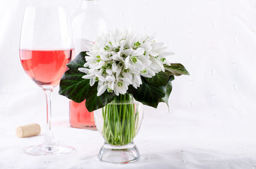 Snowdrop bouquet, white spring flowers and pink wine on light background. Copy space