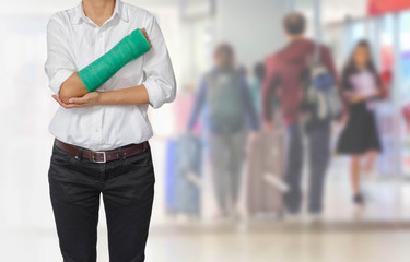 Injured woman with green cast on hand and arm on traveler in motion blur in airport interior background, ,body injury concept