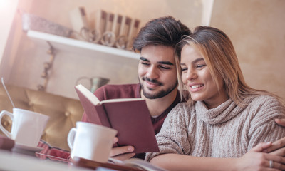 Fototapeta premium Young couple drinking coffee and reading a book in the cafe. Education, relationships, love concept