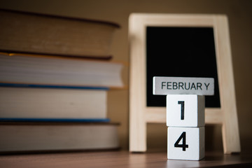 Concept for valentine or love - pile of books and chalkboard with calendar showing 14th of february in the backdrop wooden.