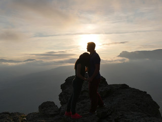 Silhouettes of young couple standing on a mountain and looking to each other on beautiful sunset background. Love of guy and girl.