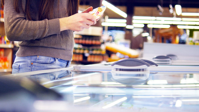 Female Hands Opening Glass Door In The Refrigerated Section At The Supermarket And Choosing Ice Cream. Young Woman Taking Product From Fridge In Shop And Putting It Into The Basket. Close Up