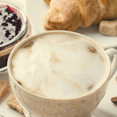 Traditional breakfast with fresh croissants and coffee on white wooden background.