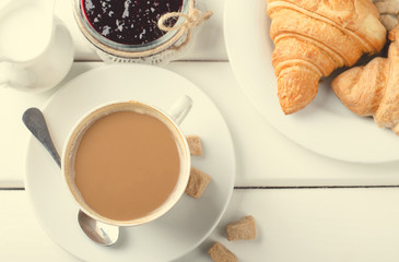 Traditional breakfast with fresh croissants and coffee on white wooden background.