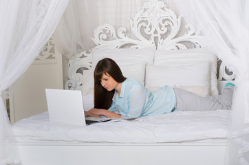 Obraz premium Woman in home clothes resting on a bed and looking at a laptop
