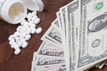 Pills and dollars. A pile of US dollars in cash and white pills or drugs. Drug concept image. Focus point on the cash.