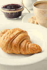 Traditional breakfast with fresh croissants and coffee on white wooden background.