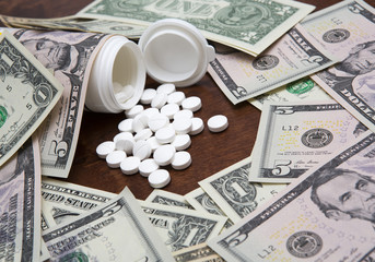 Pills and dollars. A pile of US dollars in cash and white pills or drugs. Drug concept image. 