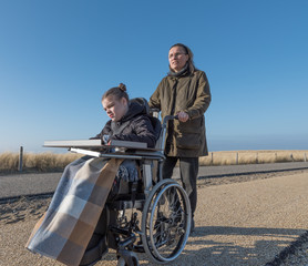 Working together with disability / A womand pushing a wheelchair with a disabled child along a...
