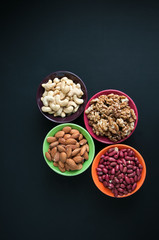 Mix of nuts in ceramic bowls on a black background. Almond, peanut, cashew and walnut.