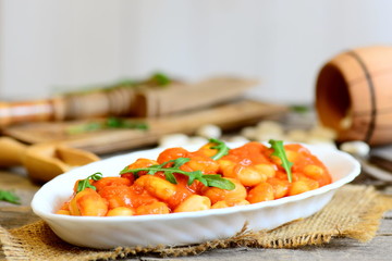 Healthy baked beans with tomato sauce served with fresh arugula on a plate. Easy slow cooked baked beans recipe. Vegan side dish. Rustic style. Closeup