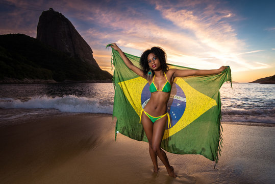 Young Beautiful and Sexy Girl in Bikini Holding Beach Yoke With Brazilian Flag by Sunrise with the Sugarloaf Mountain in the Background, in Rio de Janeiro